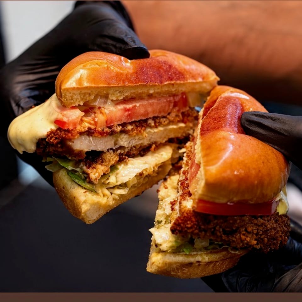 Crispy fried chicken sandwich on a brioche bun with melted cheese, tomato, and lettuce, held in two halves.