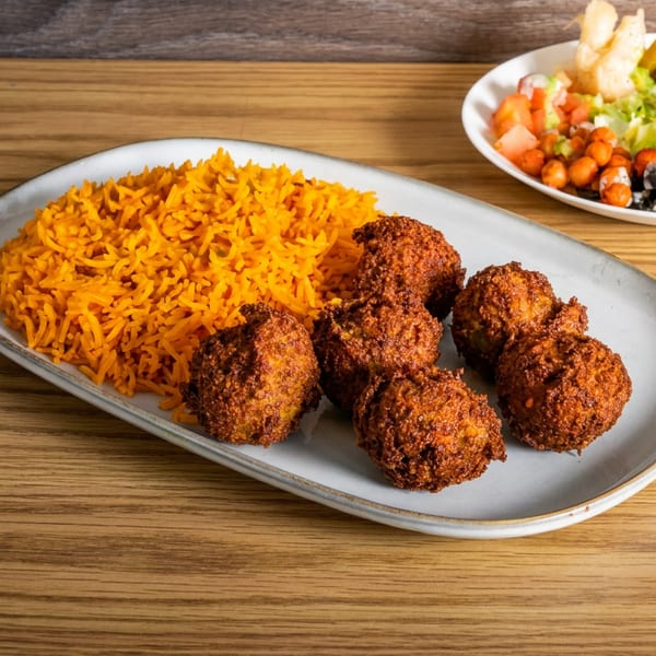 Plate of orange rice and crispy fried bean fritters with a side salad on a wooden table.