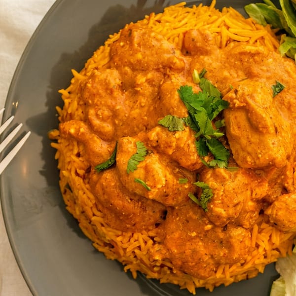 Creamy spiced chicken served over orange rice with lettuce, tomatoes, cucumbers, peppers, and a side of white sauce.